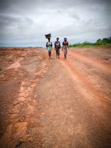 Three African women walking on a rural road in Nigeria, carrying a container.